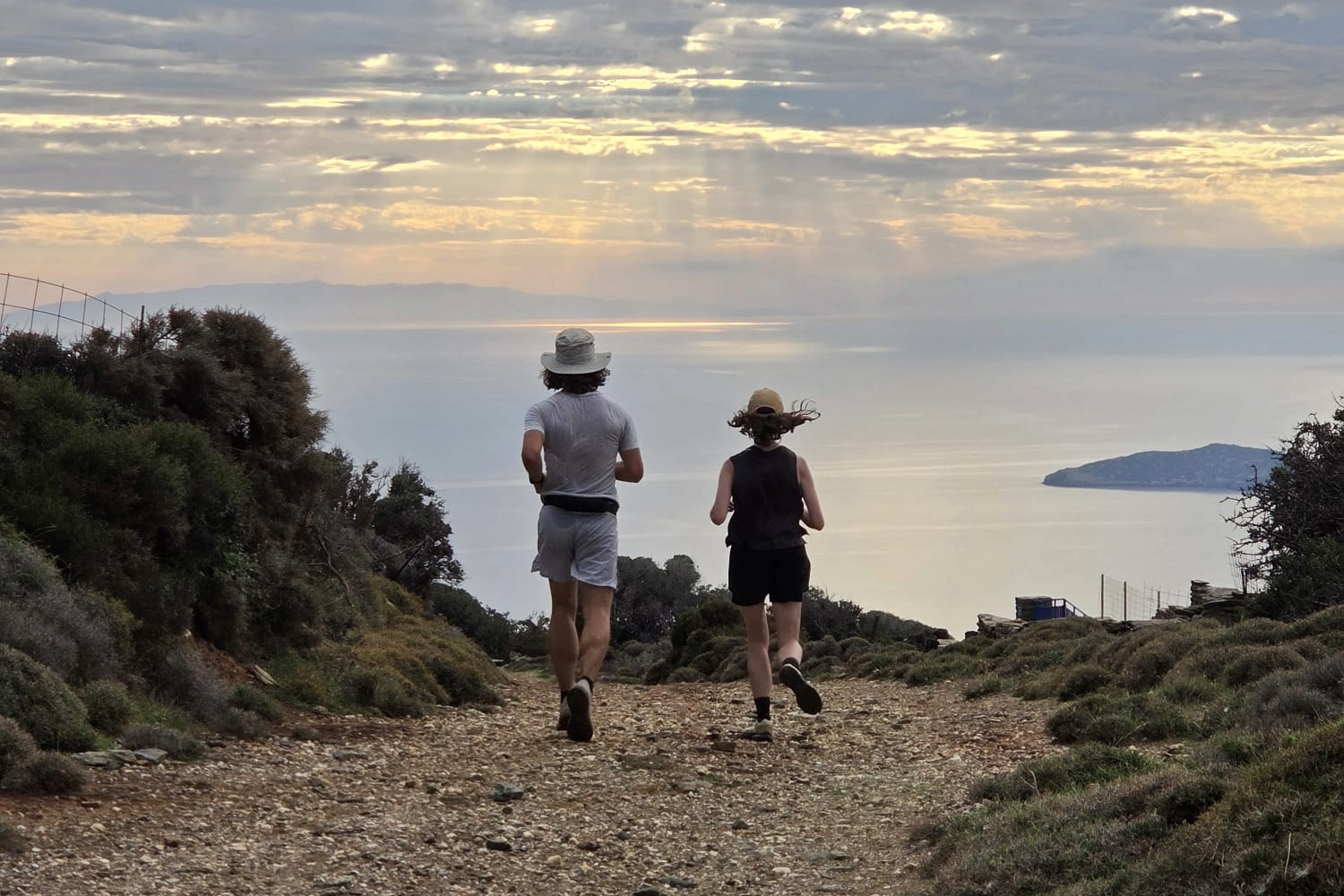 Two people trail running with the sea and sunset in the background.